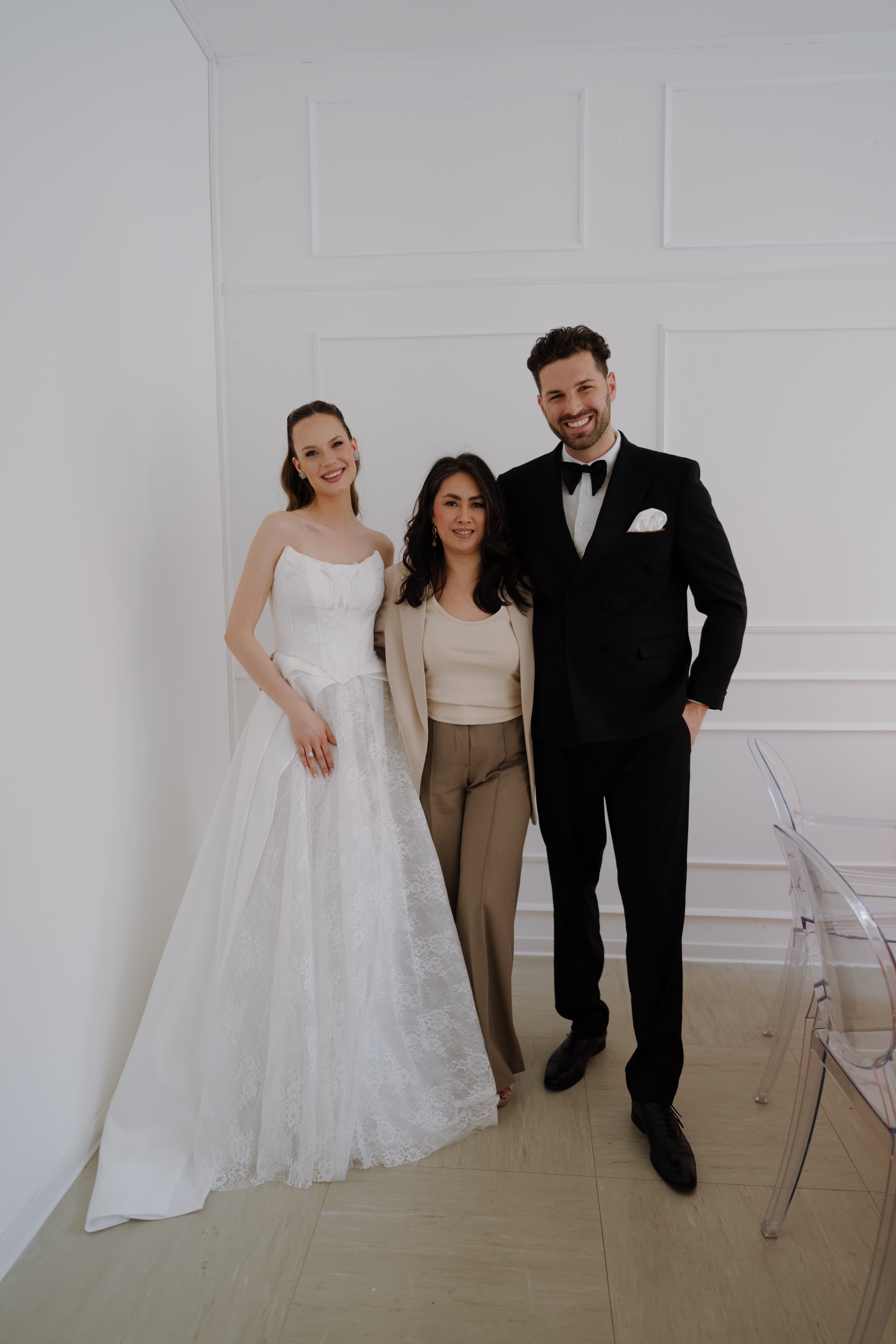 Eine Braut in einem weißen Brautkleid, eine weitere Frau und ein Bräutigam im schwarzen Smoking lächeln gemeinsam in einem Raum und feiern ihren glücklichen Tag mit einem tadellosen Service.